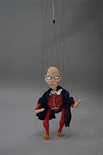 Marionette puppet carved out of wood. Older man features in the face, wearing a red outfit with a blue cape.