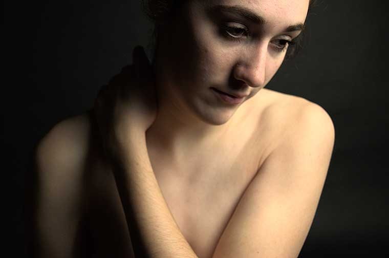 A Horizontal framed photo with the woman&#039;s face looking torn a something out of frame on the right hand size. She is holding her right shoulder with her left arm as if she is trying to massage the tenseness out of her body.