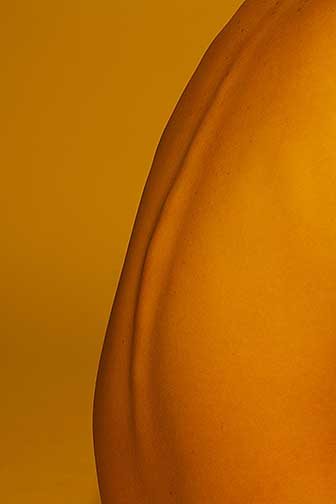 This image is of a womens tightly framed bending back with an outline of the backbone. The curve of the back starts at the bottom left corner and leaves through the top right with the subject taking up the entirety of the right bottom corner. This image has a orange color from the smooth subject to the seamless background. The subject sticks out from the background as the back has definition and roundness.