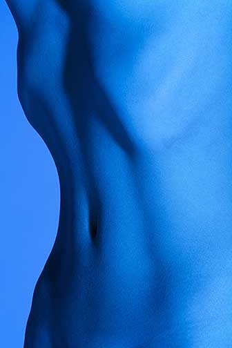 This image is of a womens tightly framed stomach from right before the vagina to the ribcage. The subject takes up the right side of the photograph leaving some negative space on the left. Her curves show from the outline of the stomach against the background and within the defined stomach. This image has the color blue from the smooth subject to the seamless background. There are many different tonal ranges within making the subject stick out from the background.