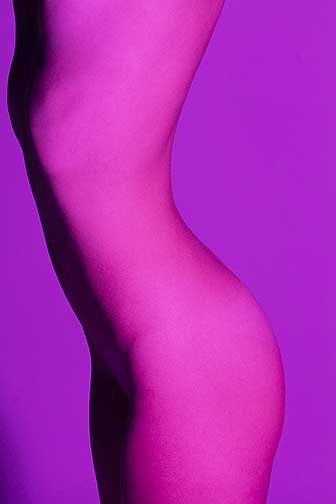 This image is a side profile of a womens twisting body from upper thigh to upper torso.The subject cuts down the middle of the photograph leaving some space on the left and right of the curving body. Curves are defined by the shadows and highlights going right to left on the skinny figure. This image has a magenta color from the smooth subject to the seamless background. The curves of the subjects back to butt and ribcage to vagina create a visual movement from top to bottom.