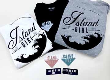 This image is sweatshirts and stickers with screen printed logos on the front and back of the sweatshirt. The logo is black and says island girl with a wave inside the circle. The stickers are blue and pink triangles saying island girl and island guy. The second set of stickers are black rounded rectangles saying island girl and island guy. 