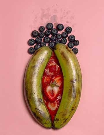 A vagina depicted with two bananas placed together, strawberries in between, and blueberries with wet stains on top.