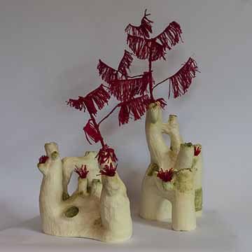 Two forms on a white background. The left form is shorter than the right. They are both organic, arrangements of tubes of varying size forming a coral like structure. All the tubes are open at the top. One tube on each structure has a red tree-like form coming out of it vertically. Several tubes have tufts of red thread, matching the tree forms, coming out of them.