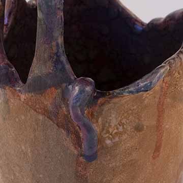 ​​​​​​​Image c: A detail of the wormy form on the previous vessel. The blue and purple blotches are pronounced against the orange. The mottled glaze texture is more visible in this Image.