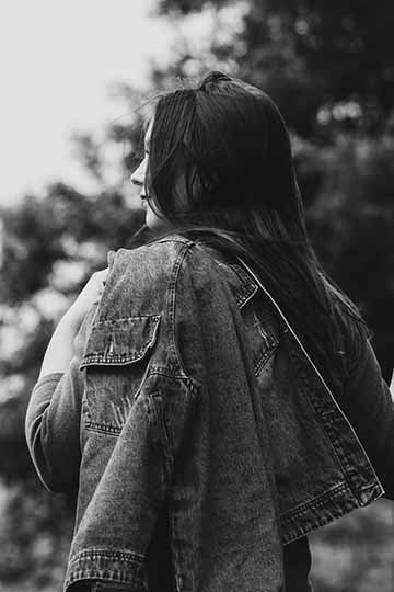 The photograph is a black and white medium shot of a female subject looking off to the left with a jean jacket draped over her left shoulder. 
