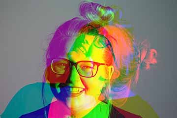 The photograph is a colored close up shot of a female model that incorporates two photographs laying over each other to create a double exposure photograph. Double exposure is “the repeated exposure of photographic plate or film to light, often producing ghost images.” The female model is laughing in both images. The image in the background is the female model laughing, looking away from the camera focusing on above and slightly leaning back off of a stool in a studio space. The photograph that lays over to