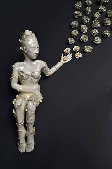 This ninety piece ceramic set consists of one figurative sculpture and various shaped and scaled vessels. The body of work begins with an all white semi nude female figure laying on the ground with her eyes closed and one hand reaching out. Over her body grows floral-like petals and moves in one general direction towards the extended hand. In her hand is one pure white flower. From her hand the vessels start to emerge and grow away from her and in an upwards direction. As we move away from the vessels close
