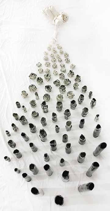 This ninety piece ceramic set consists of one figurative sculpture and various shaped and scaled vessels. The body of work begins with an all white semi nude female figure laying on the ground with her eyes closed and one hand reaching out. Over her body grows floral-like petals and moves in one general direction towards the extended hand. In her hand is one pure white flower. From her hand the vessels start to emerge and grow away from her and in an upwards direction. As we move away from the vessels close