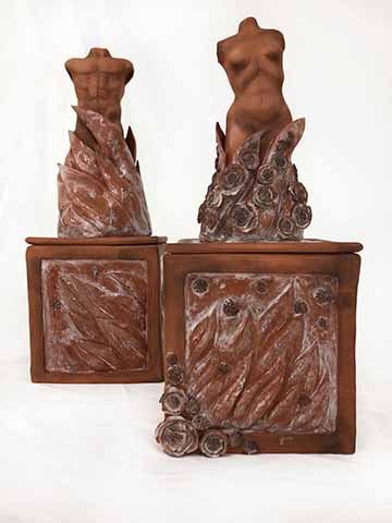 This ceramic work displays two adorned boxed or pedestals, one with the torso of a female body placed centrally on top of the structure and the other of a male. On both pieces there are abstract fire-like forms flowing and consuming the lower portion of both the male and female body. One the female sculpture we see delicate flowers flowing up and around the piece. On the male sculpture, carved stars match the placement of where the flowers fall on the other work. The color scheme is simple, letting the natu