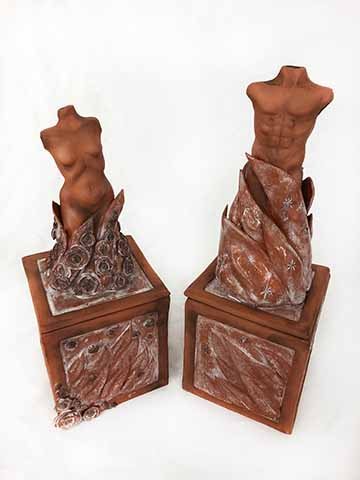 This ceramic work displays two adorned boxed or pedestals, one with the torso of a female body placed centrally on top of the structure and the other of a male. On both pieces there are abstract fire-like forms flowing and consuming the lower portion of both the male and female body. One the female sculpture we see delicate flowers flowing up and around the piece. On the male sculpture, carved stars match the placement of where the flowers fall on the other work. The color scheme is simple, letting the natu